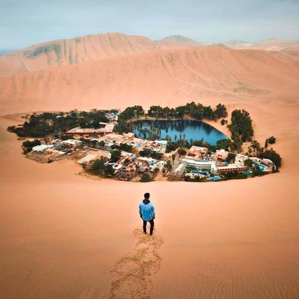 Spectacular panoramic view of Huacachina Oasis surrounded by towering desert dunes in southern Peru.