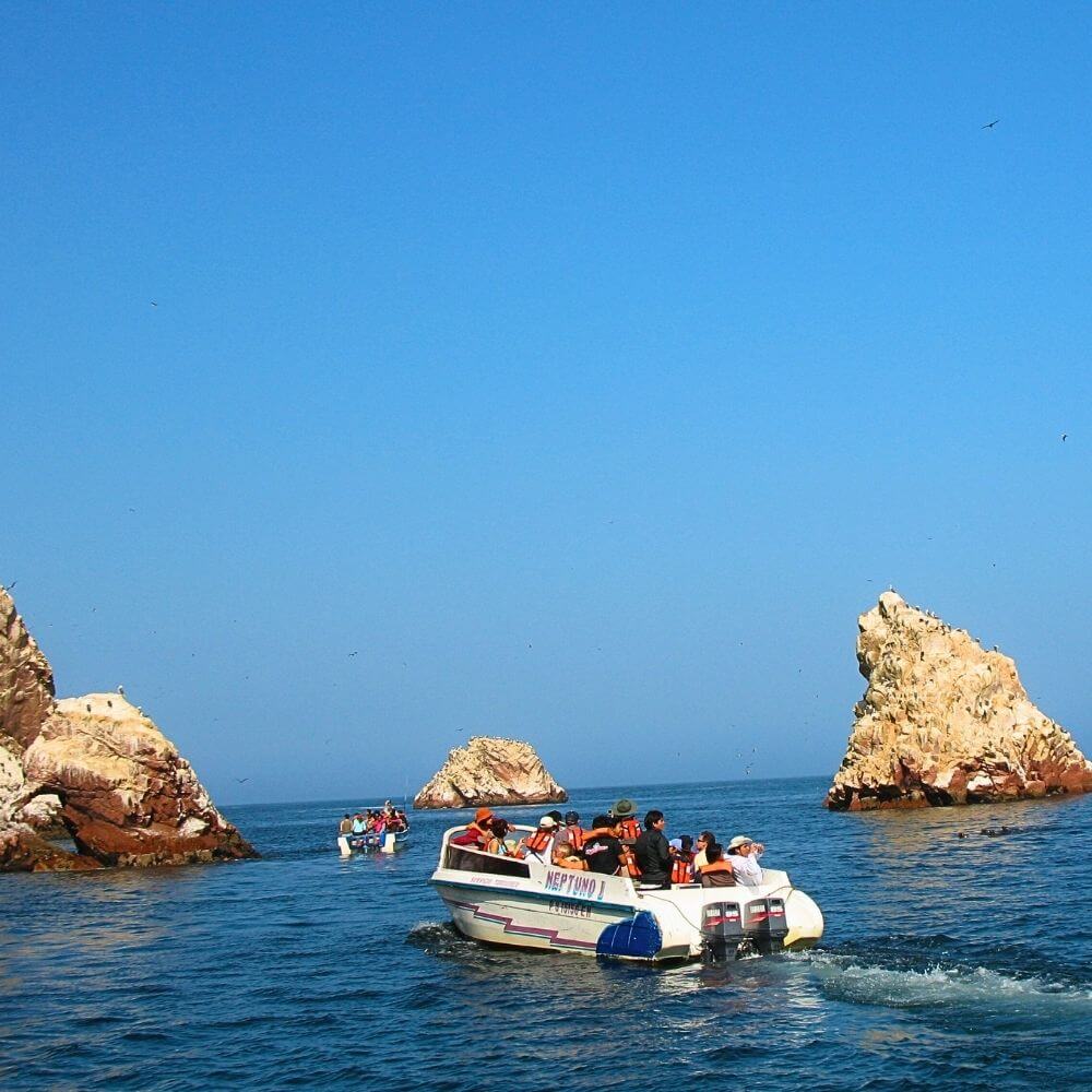 Tour boat navigating among the rocky formations of the Ballestas Islands, famous for marine wildlife and sea birds.