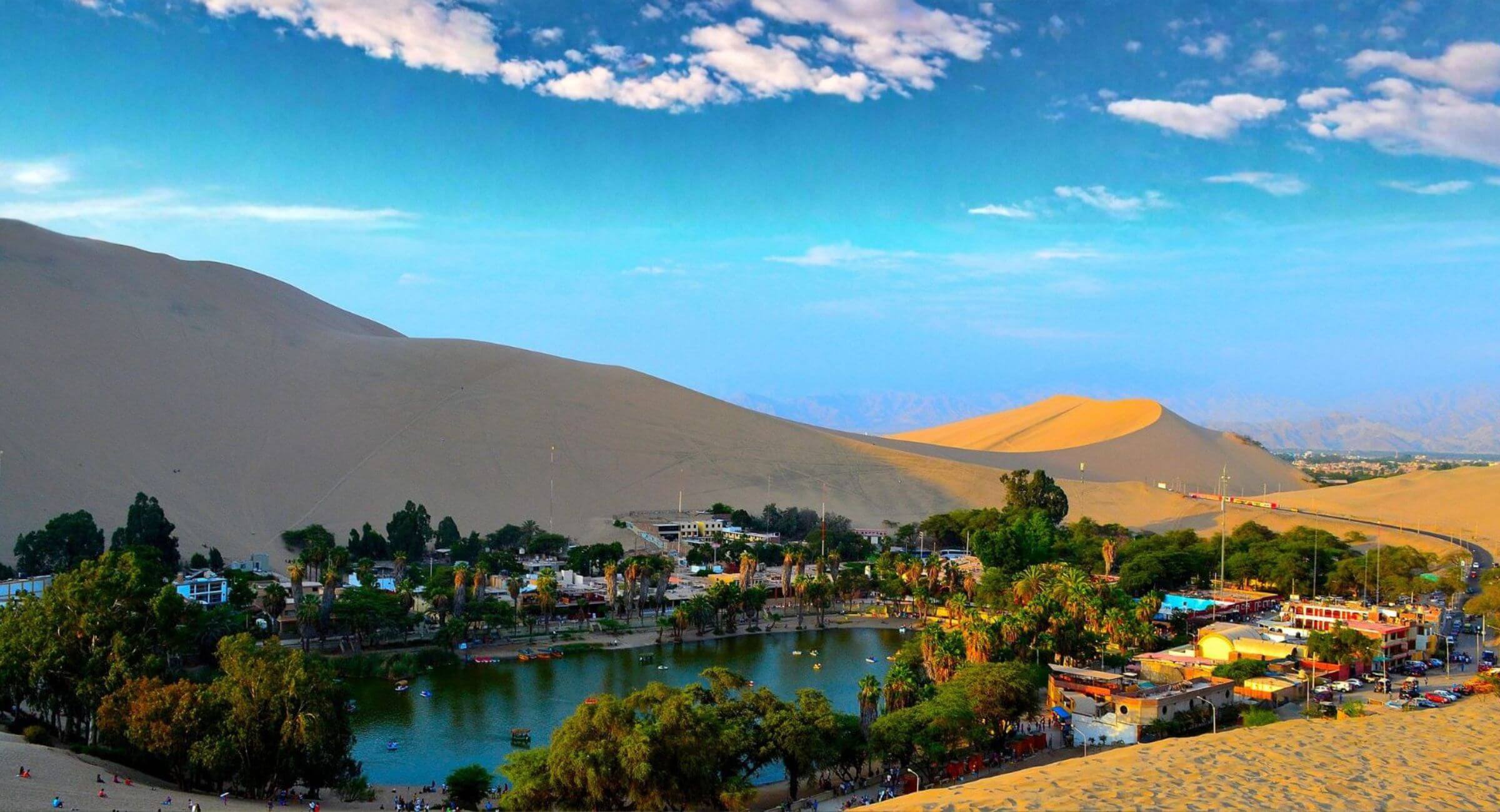 Huacachina oasis lagoon surrounded by palm trees and giant sand dunes