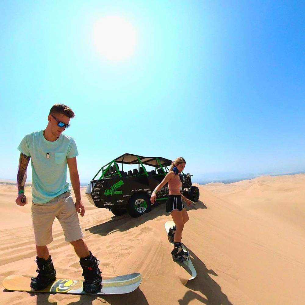 Travelers sandboarding down the golden dunes of Huacachina during an exciting desert adventure in Peru.