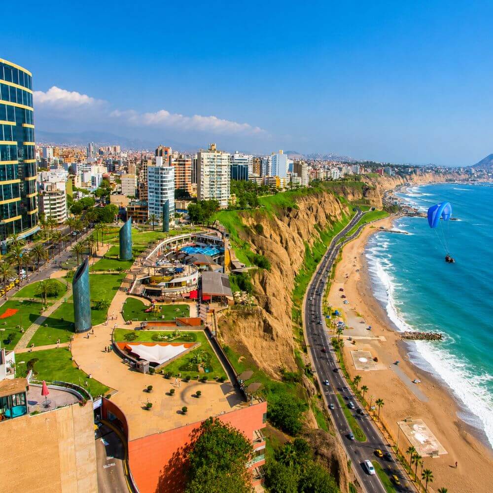 Panoramic view of Miraflores, Lima's coastal cliffs, Pacific Ocean beaches, and paragliding over the shoreline.