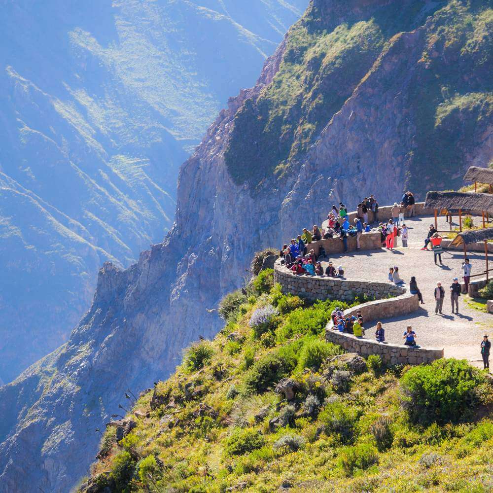 Travelers enjoying panoramic views from Cruz del Condor overlooking the dramatic Colca Canyon during the Colca Canyon Tour from Puno.
