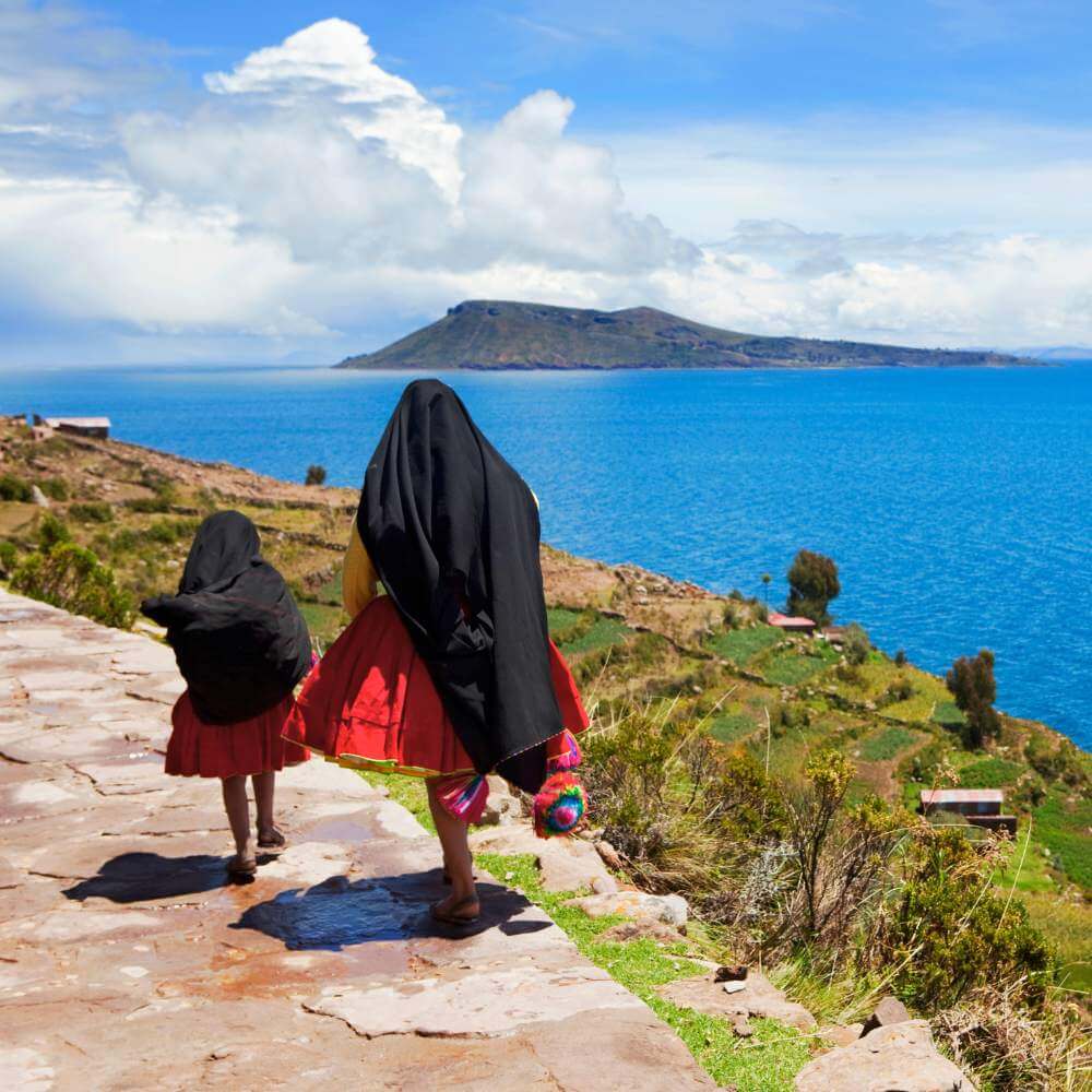 Islander walking along a scenic trail on Taquile Island overlooking Lake Titicaca during a Lake Titicaca Full Day Tour.