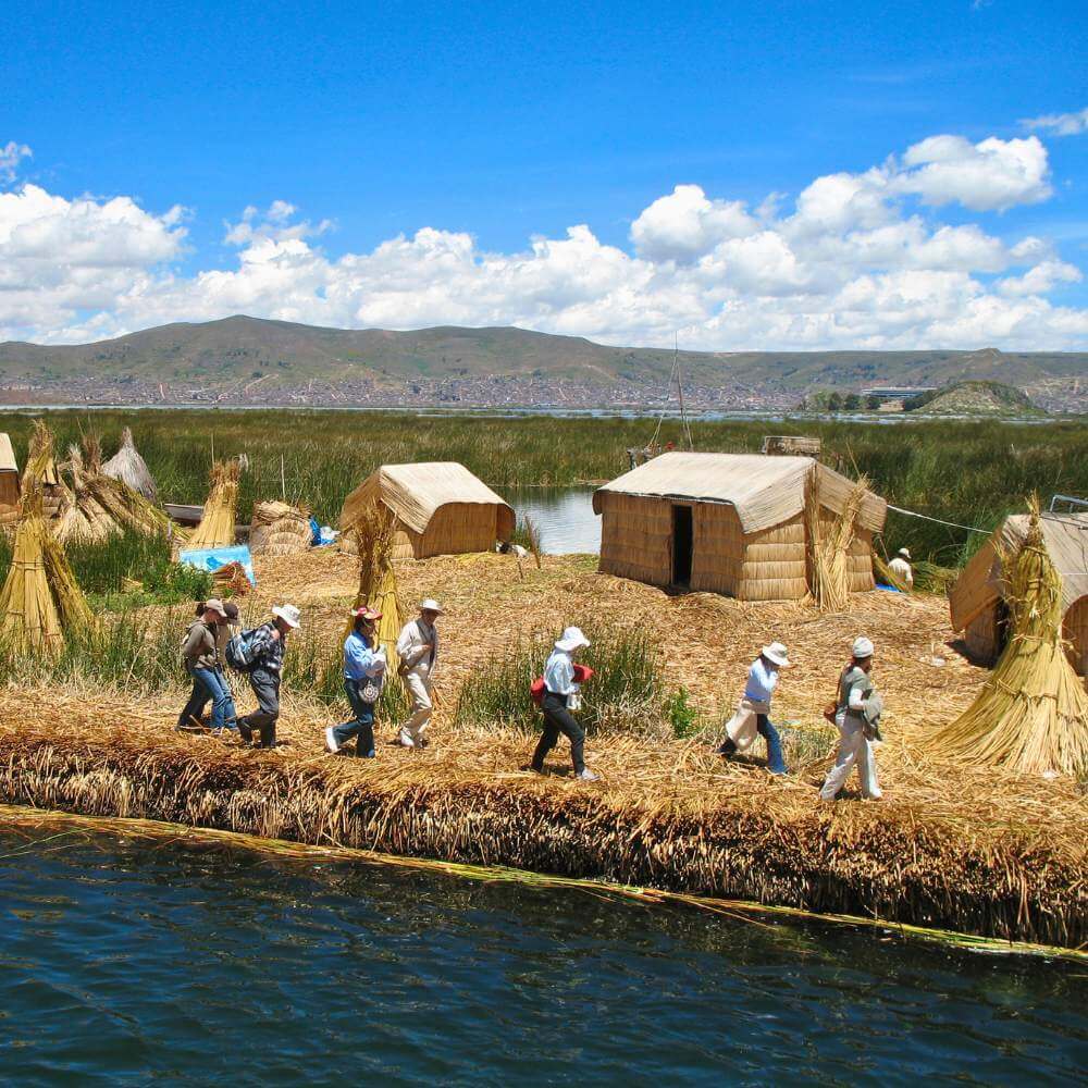 Visitors exploring the Uros Floating Islands during a Lake Titicaca Homestay Tour in Peru, surrounded by traditional reed houses and breathtaking lake scenery.