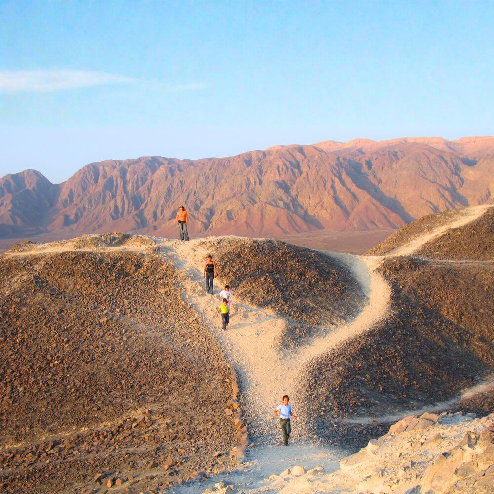 Visitors walking through the Nazca Desert landscape surrounded by mountains during a Nazca Lines land tour in Peru.