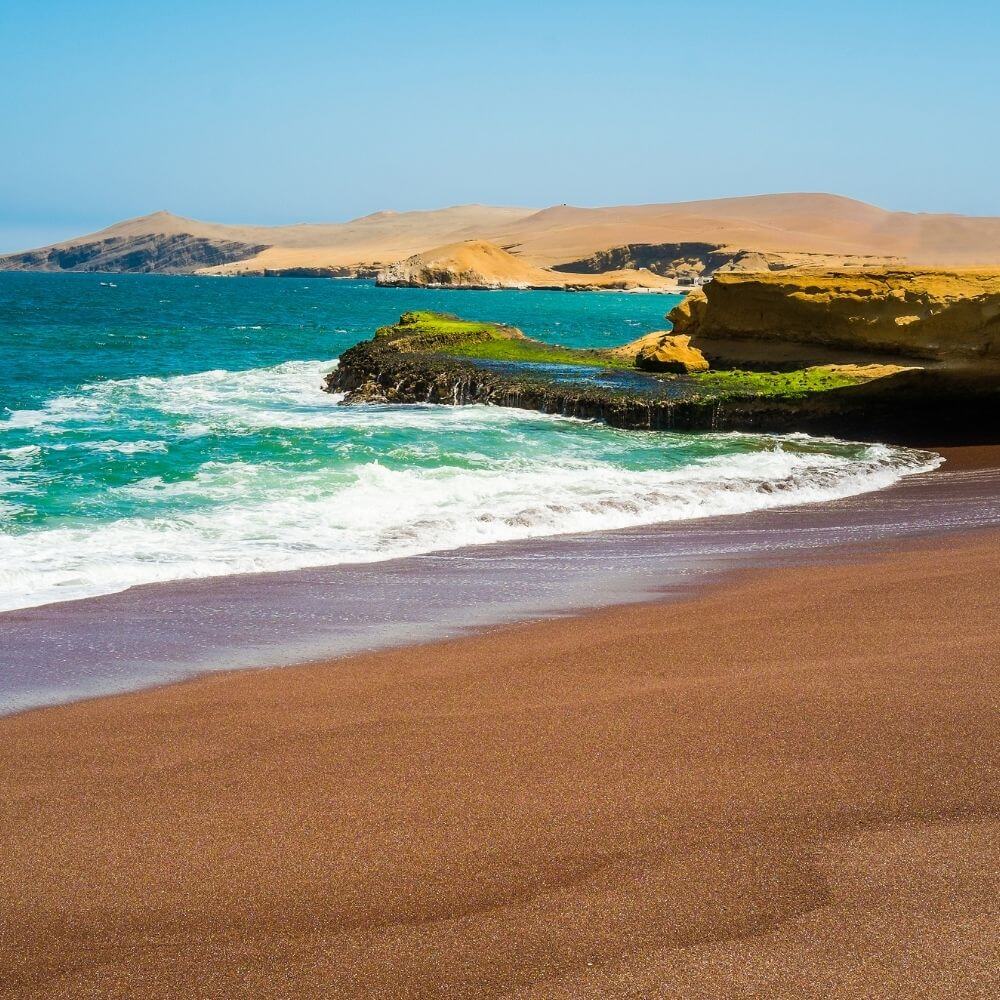 Red Beach in Paracas National Reserve with colorful sands, ocean waves, and dramatic desert coastline.