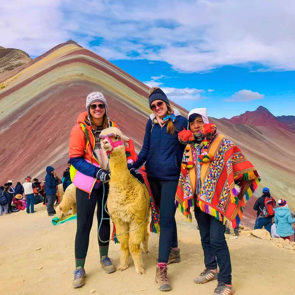 Travelers posing with a local Andean guide and alpaca at Rainbow Mountain during a trekking tour from Cusco.