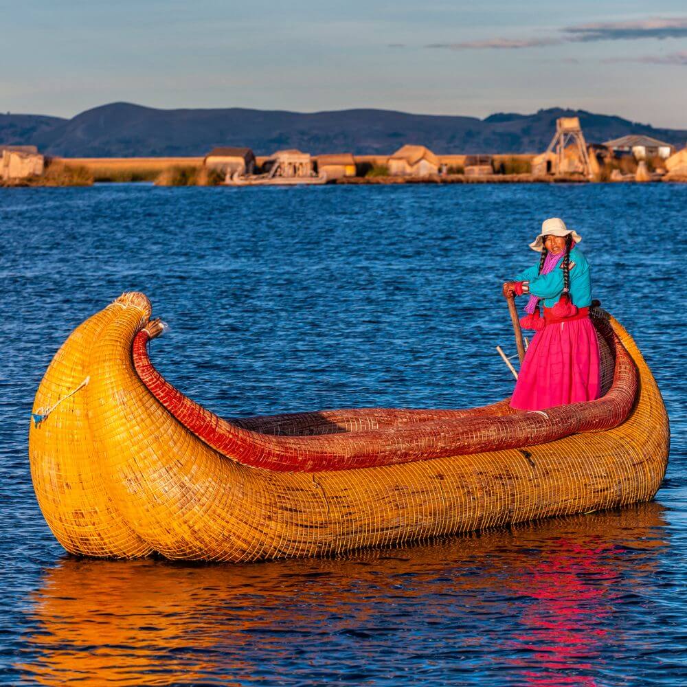 Traditional totora reed boat with a Uros woman navigating the waters of Lake Titicaca near the floating islands in Peru.