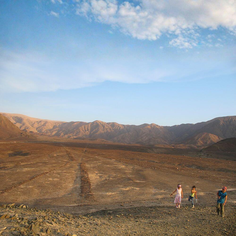 Travelers walking among the ancient Nazca geoglyphs in the zone of Cantalloc near Nazca, Peru, with mountains in the background.