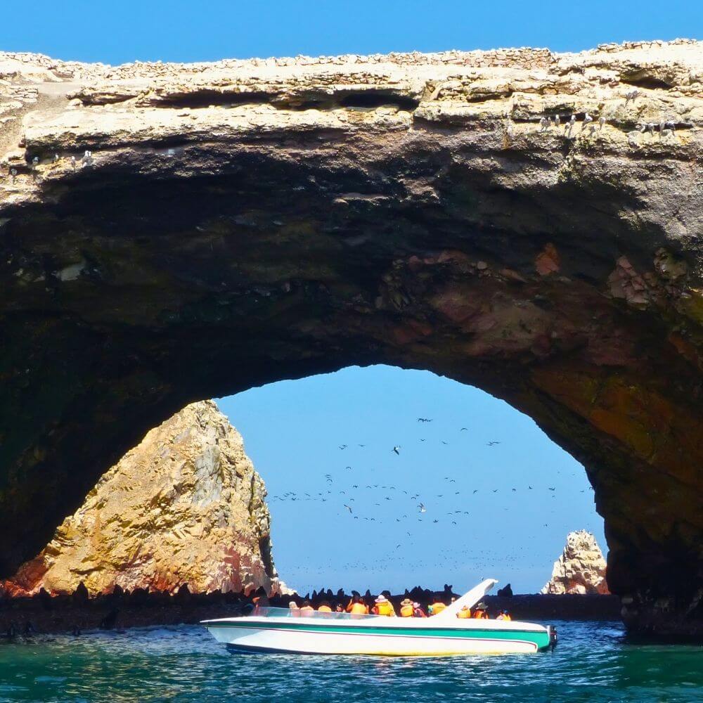 Speedboat passing through a natural rock arch at the Ballestas Islands during a wildlife tour from Paracas, Peru.