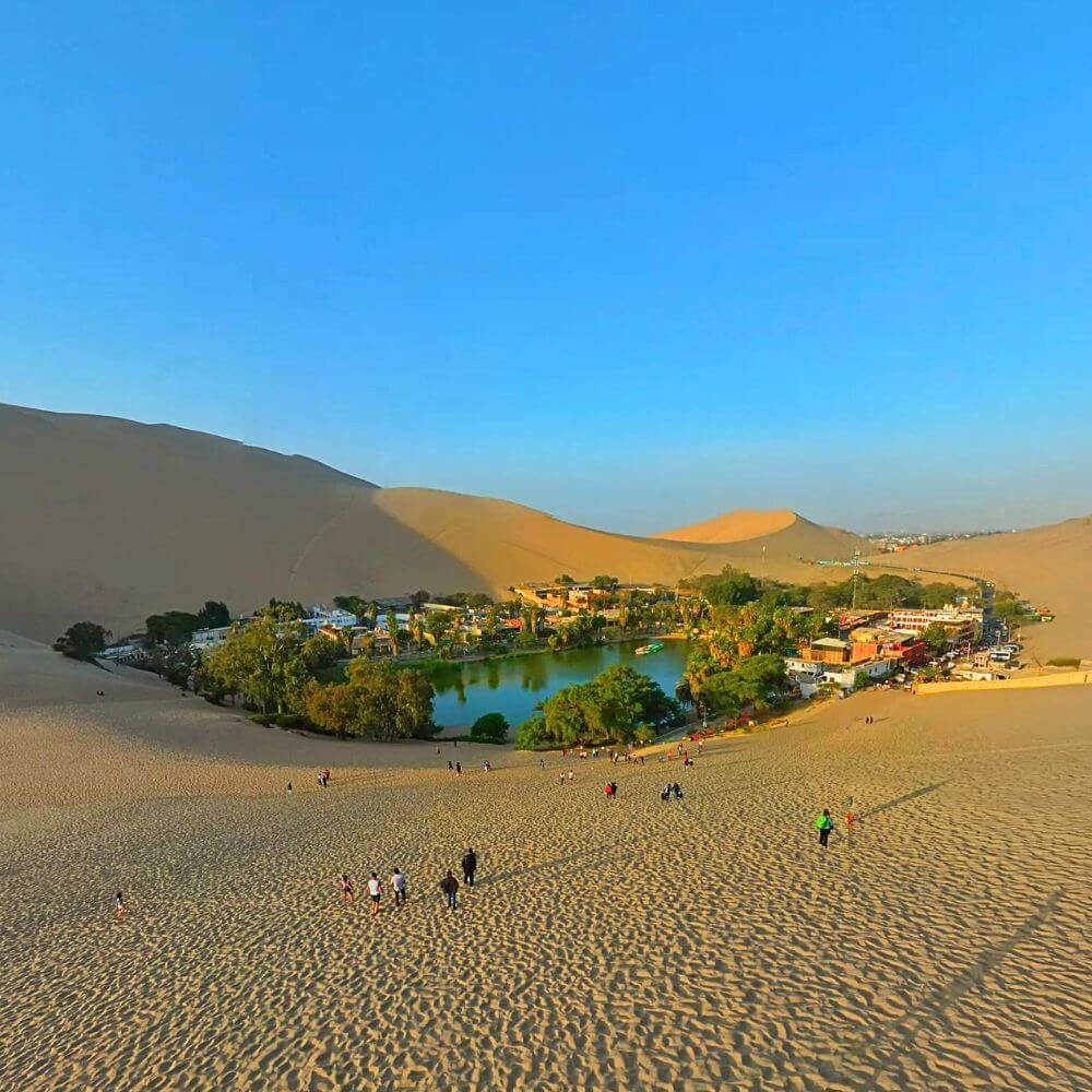 Panoramic view of the Huacachina Oasis surrounded by giant sand dunes in the Ica Desert of Peru.