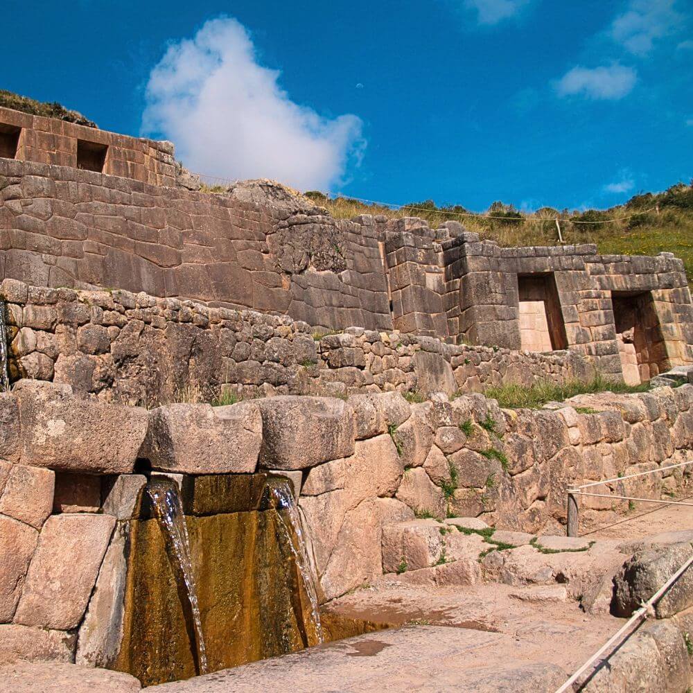 Flowing water channels and finely crafted stone walls at Tambomachay archaeological site near Cusco.