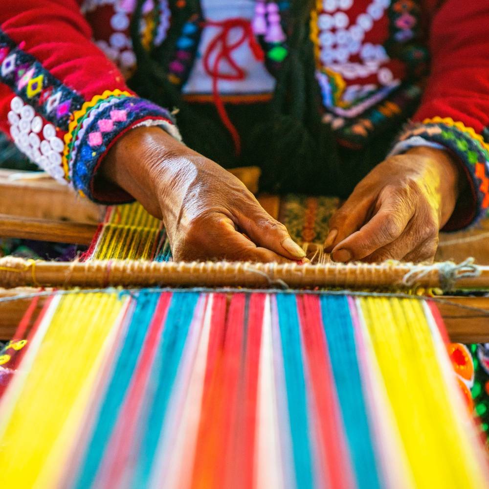Andean artisan weaving colorful alpaca textiles using traditional techniques at Awana Kancha in the Sacred Valley.