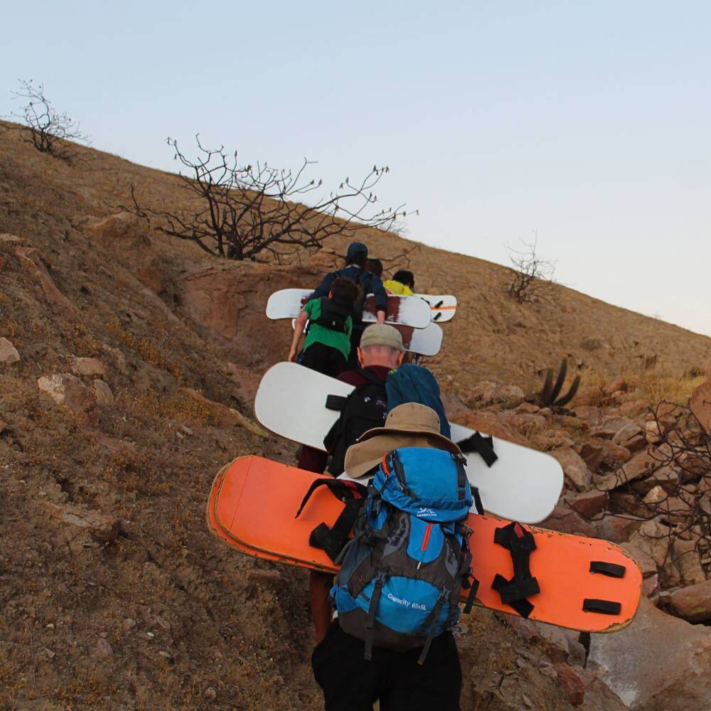 Adventure travelers crossing the massive ridges of Cerro Blanco during a sandboarding expedition in Peru.