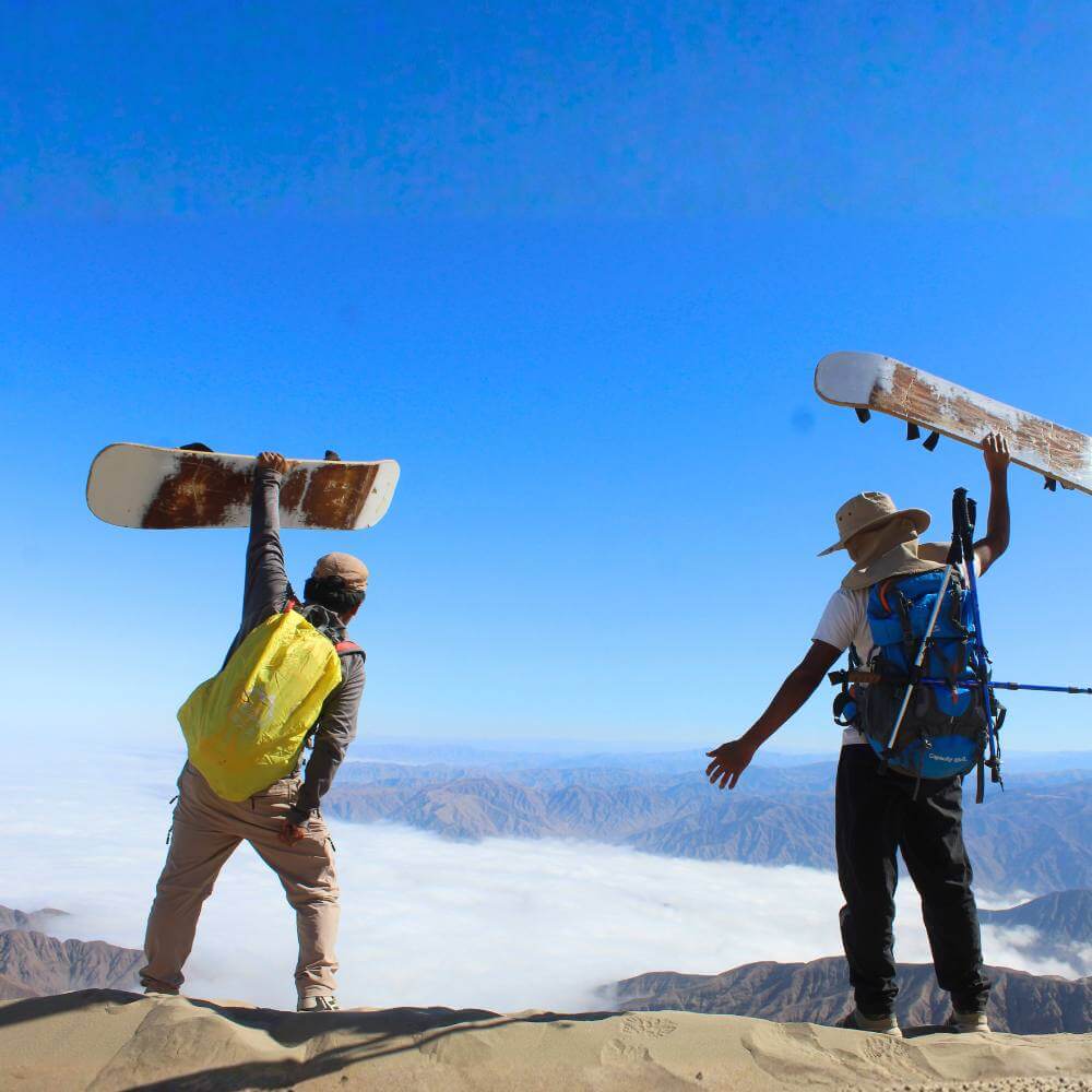 Local guides standing on the summit of Cerro Blanco holding sandboards above a sea of clouds in Nazca.