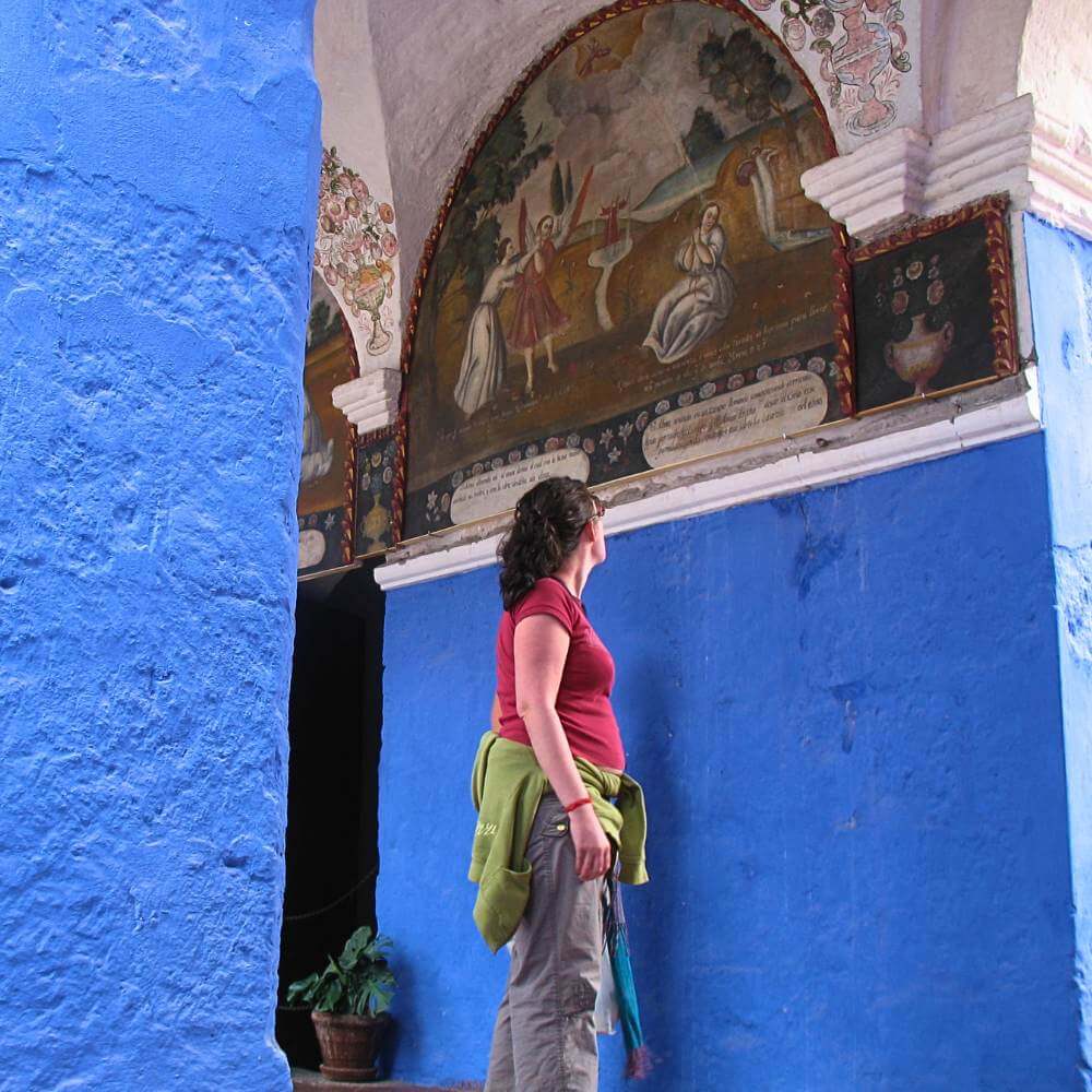 Traveler admiring colorful colonial corridors and historic artwork inside Santa Catalina Monastery in Arequipa, Peru.
