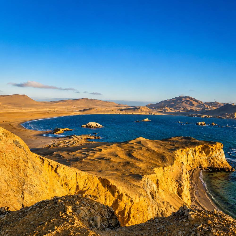 Panoramic view of the dramatic coastal cliffs, desert dunes, and turquoise bay in Paracas National Reserve during the Golden Shadows Trek.
