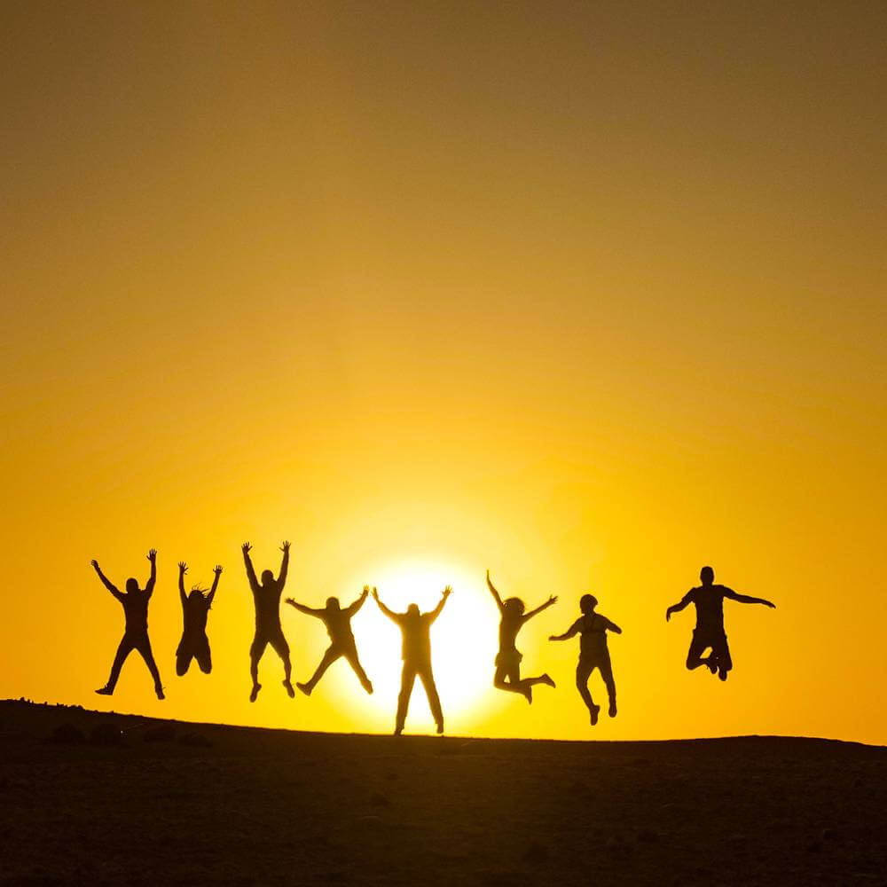 Travelers celebrating at sunset on the Golden Shadows Trek in Paracas National Reserve with panoramic Pacific Ocean views.