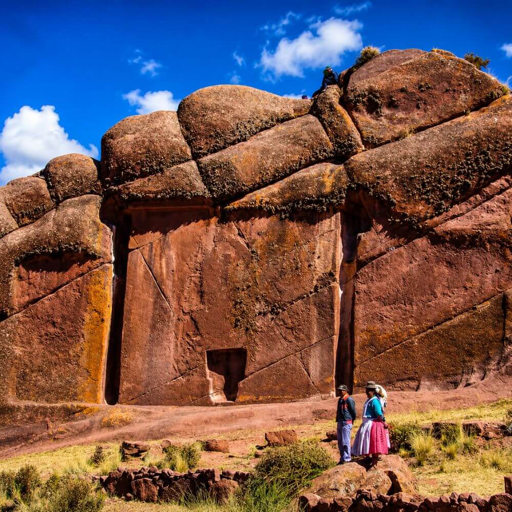 The ancient carved stone doorway of Aramu Muru with local Andean visitors beneath the monumental rock formation near Lake Titicaca, Puno, Peru.