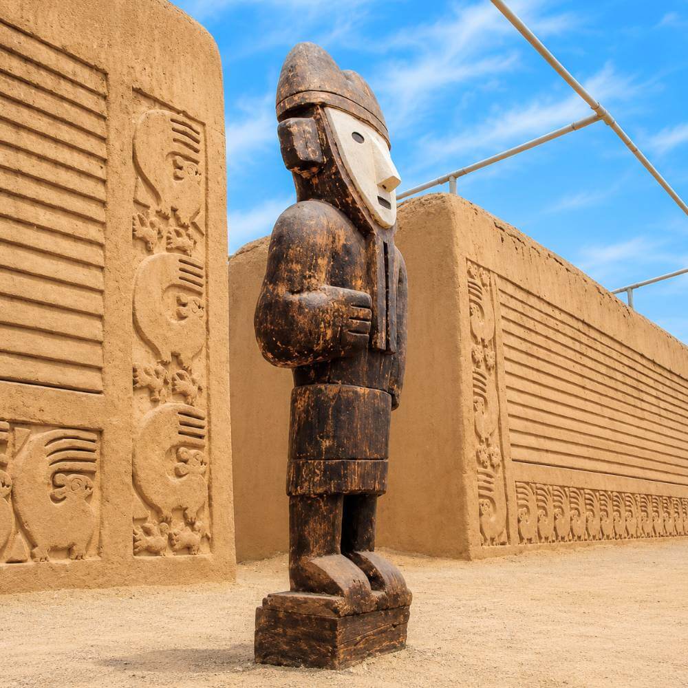 Ancient Chimú guardian statue surrounded by intricately carved adobe walls at Chan Chan Ruins, UNESCO World Heritage Site in Trujillo, Peru