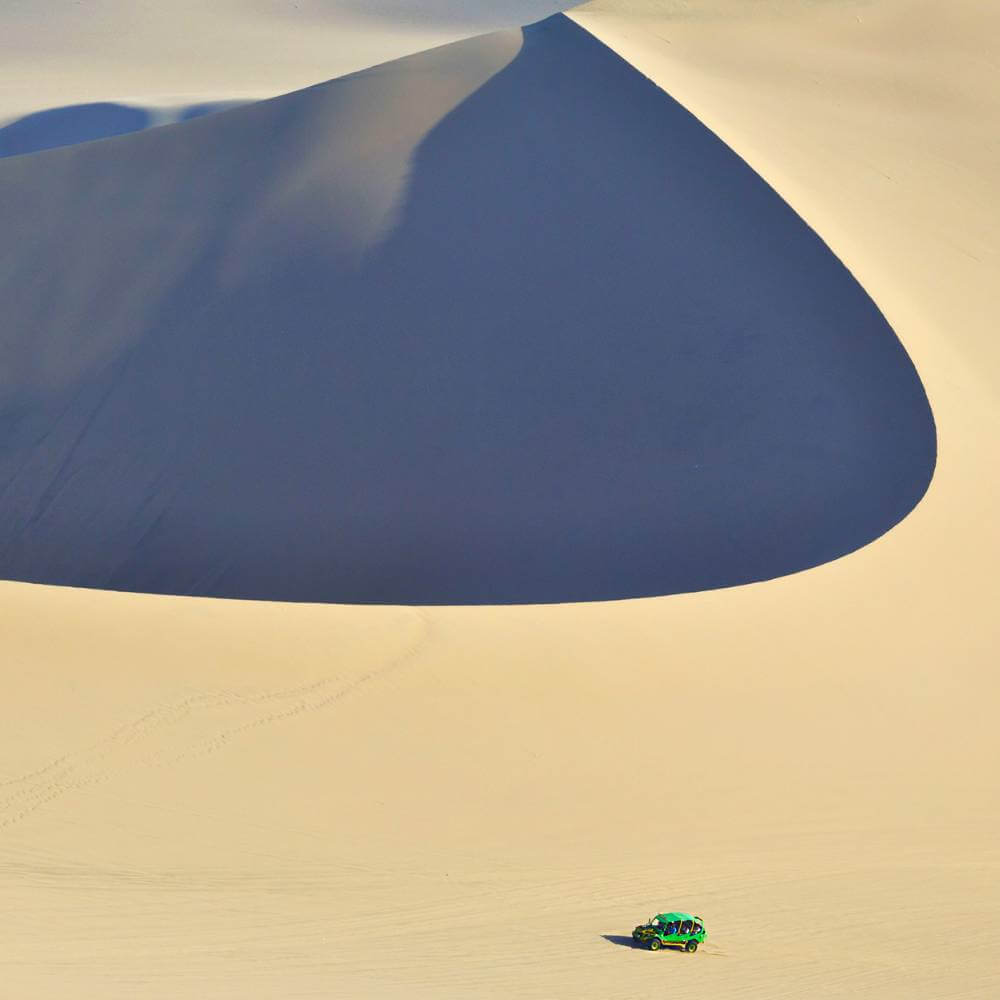 Dune buggy crossing the massive sand dunes of the Huacachina Desert in Peru with dramatic desert scenery.