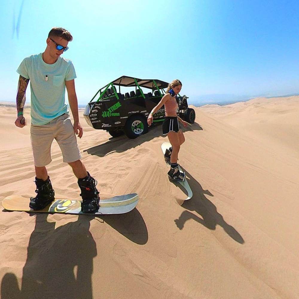 Travelers enjoying sandboarding on the towering dunes of Huacachina during a dune buggy adventure in Peru.