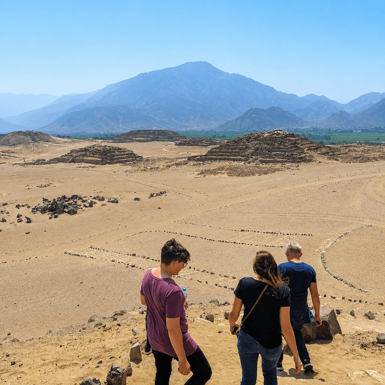 Travelers walking through the ancient ruins of Caral with panoramic views of the Supe Valley and surrounding Andean foothills in Peru.