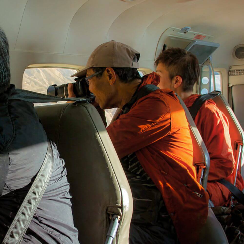 Passengers observing and photographing the Nazca Lines from inside a sightseeing aircraft during a Nazca Lines flight experience in Peru.