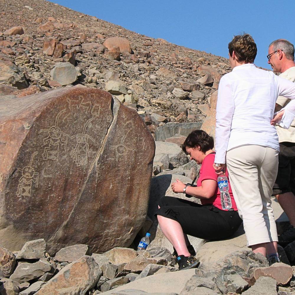 Travelers exploring ancient petroglyphs carved into volcanic boulders at the Chicchitara archaeological site near Nazca, Peru.