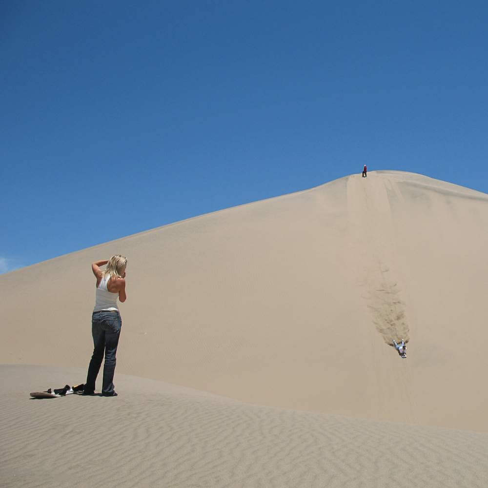 Traveler photographing the spectacular giant sand dunes of the Usaka Desert while enjoying the scenic landscapes of the USAKA DESERT TOUR.