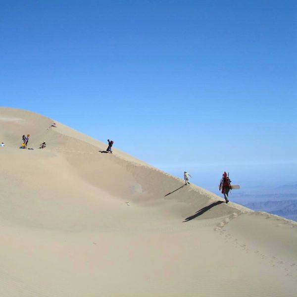 Hikers climbing Cerro Blanco dune for sandboarding adventure in the Andes