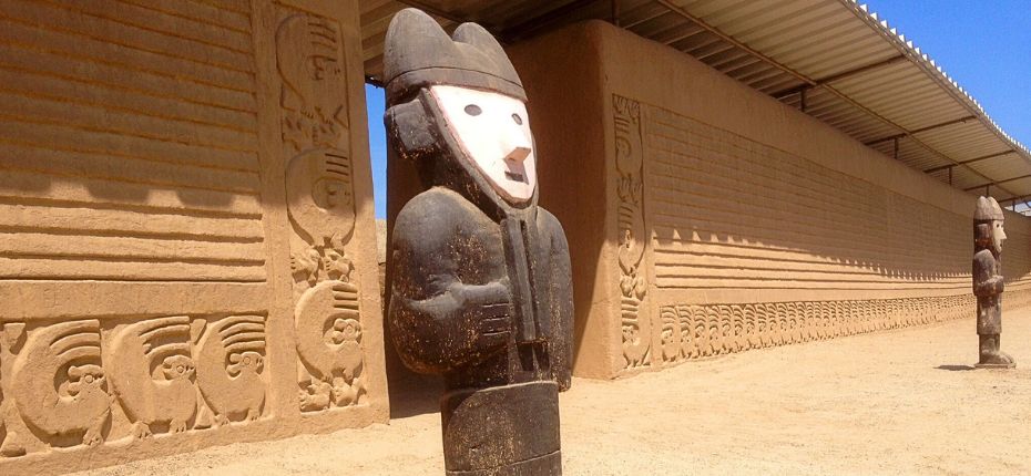 Wooden guardian statue and intricate friezes at Chan Chan Ruins.