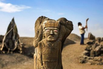 Wooden Moche sculpture at Huaca Cao Viejo with guide in the background