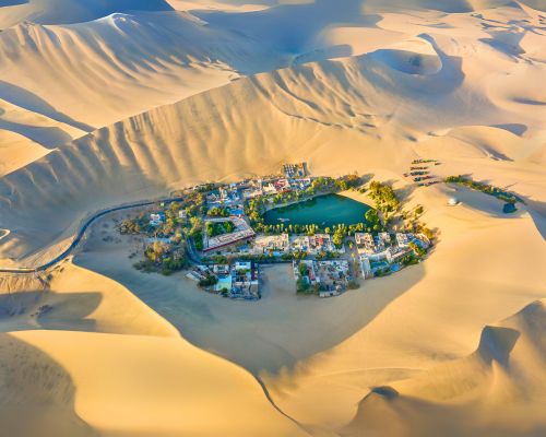 Aerial view of Huacachina Oasis surrounded by golden sand dunes