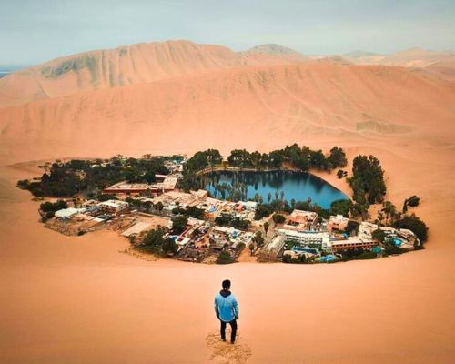 Tourist admiring Huacachina Oasis from the top of a sand dune