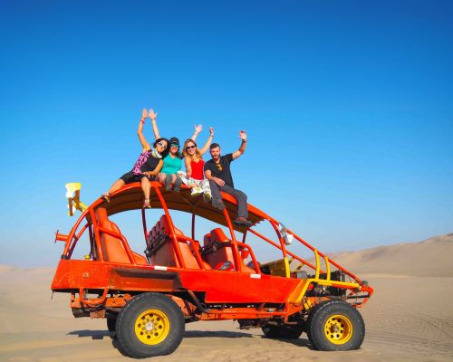 Friends posing on top of a red dune buggy in Huacachina desert