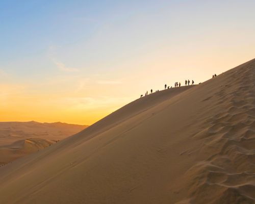 Tour group walking on sand dunes at sunset in Huacachina desert