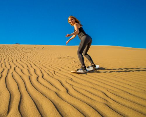 Young woman sandboarding down a golden dune in Huacachina