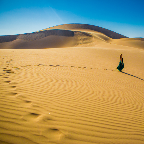 Traveler walking across the vast desert dunes of Huacachina
