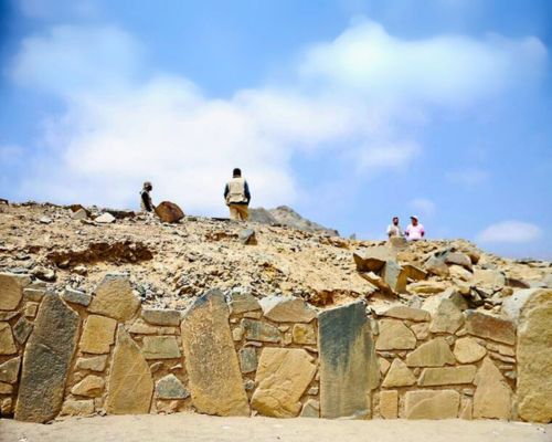 Ancient stone wall with visitors exploring the Caral ruins above