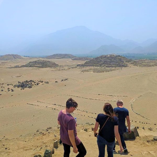 Tourists walking among the ancient ruins of Caral with pyramids in the background
