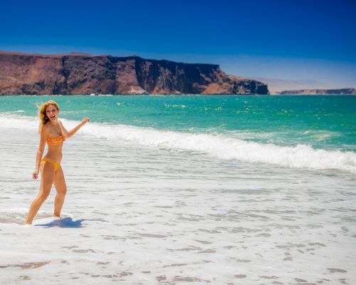 Tourist enjoying the waves on a Paracas beach with cliffs in the background