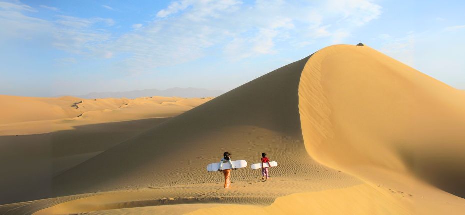 Exploring the vast sand dunes of the Usaka Desert with sandboards in hand