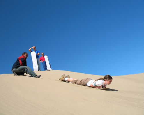 Child sandboarding on the dunes during the Usaka Desert Tour