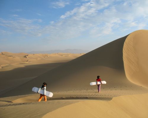 Adventurers hiking the Usaka dunes with sandboards