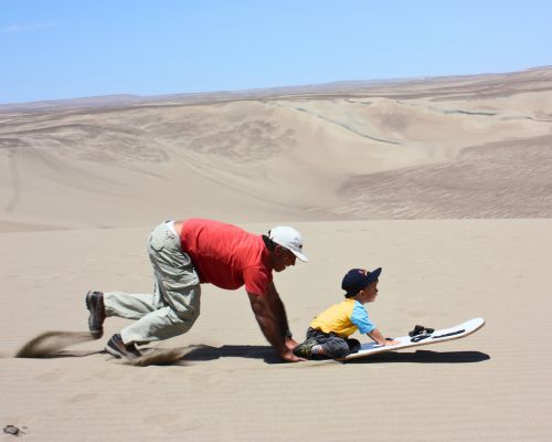 Father and son sandboarding together on the Usaka Desert Tour