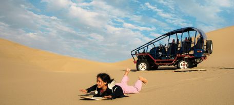Young traveler enjoying sandboarding in the Usaka Desert dunes