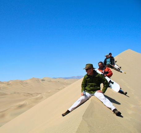 Group of adventurers preparing to sandboard down the towering dunes of Usaka